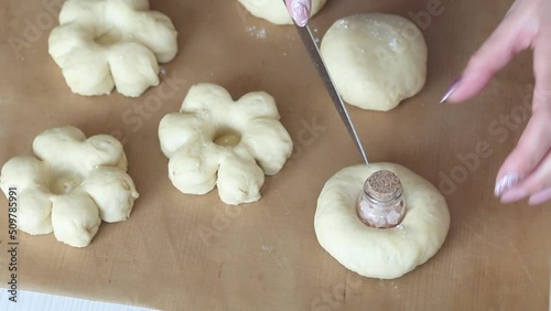 The woman shapes the dough into a flower shape. Cuts a lump of dough with a knife. Preparing donuts in the form of a flower. Close-up photo