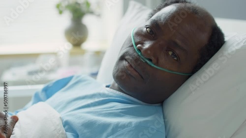 Portrait of sick African American man with nasal cannula lying on bed in hospital ward and looking at camera photo