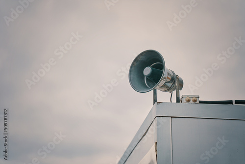 Megaphone on cloudy sky background. Providing security in town, notification of emergencies. Emergency alert siren. City hazard warning system. Copy space for text.
