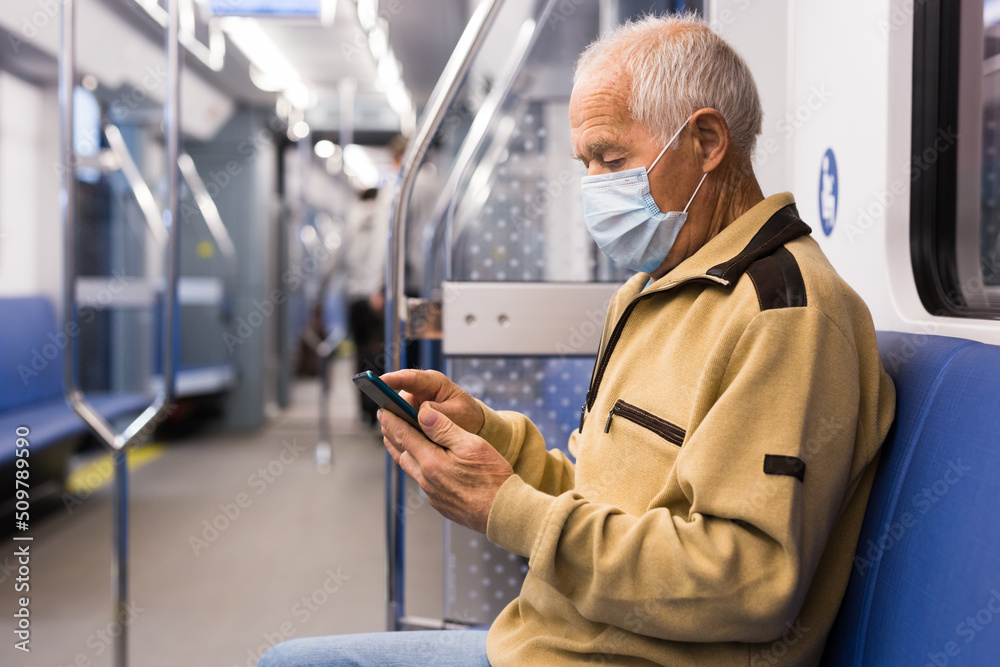 Old man in mask sitting in subway car with smartphone Old man in mask sitting in subway car with smartphone