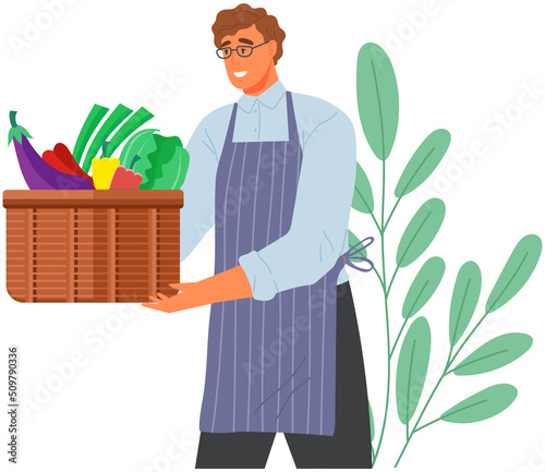 Man holding container with natural fresh food. Healthy food, proper nutrition, eating fruits and vegetables. Diet, weight loss concept. Guy in apron with basket of vegan ingredients in his hands