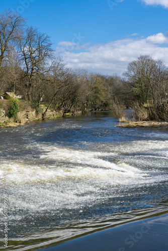 фотографія Flowing white water with bare trees in the backdrop seen downstream of a weir on the River Aire, Shipley, West Yorkshire, England, UK