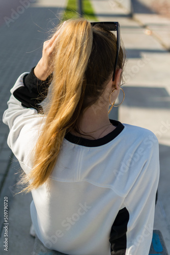 Back view of a young pretty girl in summer sunny day on street
