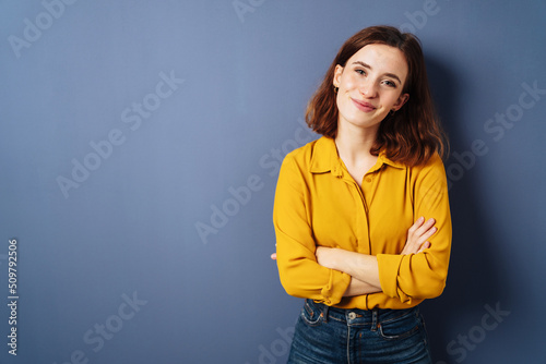 Woman standing with folded arms in front of blue background with copy space © contrastwerkstatt