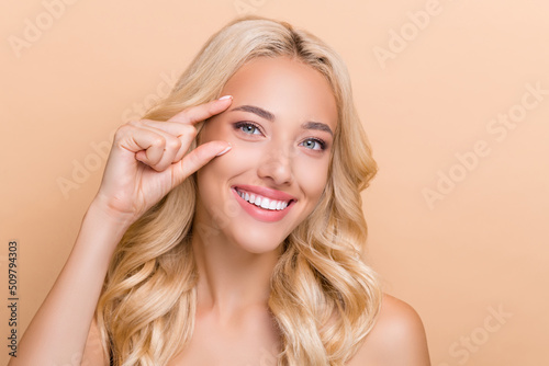 Portrait of attractive cheerful wavy-haired girl showing place injection uplift effect isolated over beige pastel color background