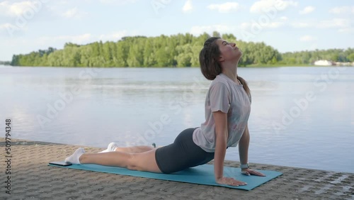 a young girl is doing yoga on the shore on the yoga mat of the river in the evening