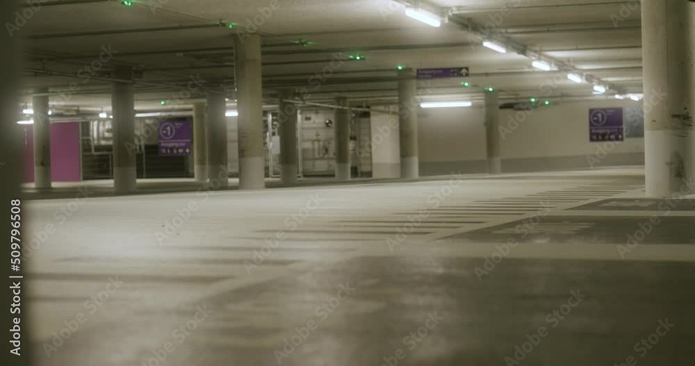 View of black male walking in across screen into empty underground parking lot with bright lights in Metzingen, Germany, Baden Wurttemberg, Europe, panning view angle View of black male walking in across screen into empty underground parking lot with bright lights in Metzingen, Germany, Baden Wurttemberg, Europe, panning view angle