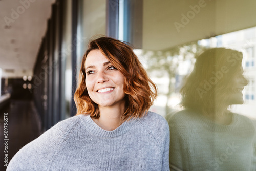 Woman leans against a glass pane and looks to the side laughing photo