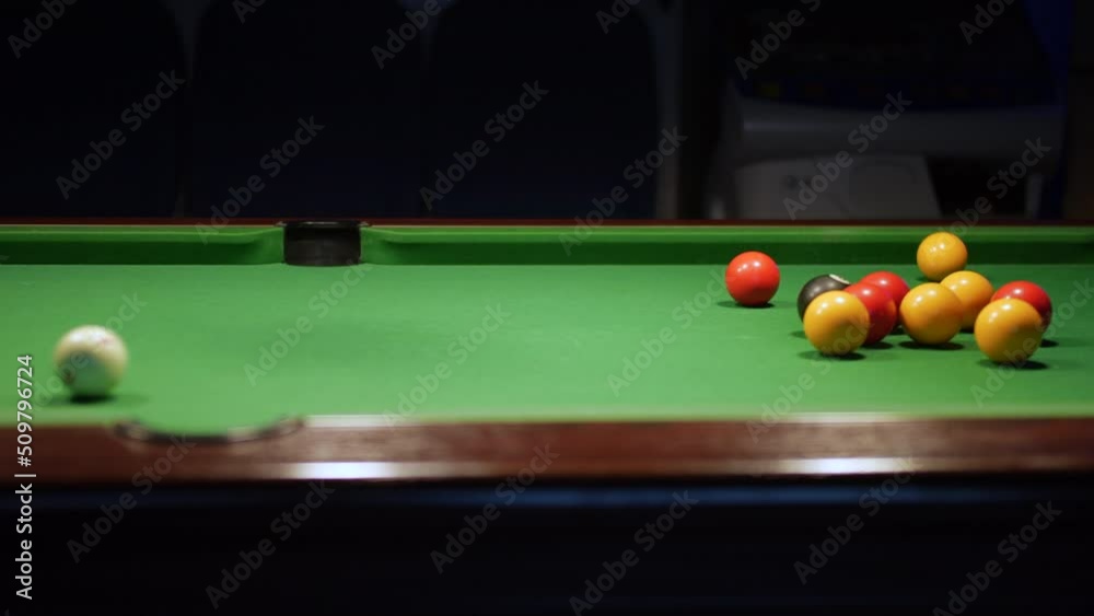 Potting a red ball in to a center pocket on a green pool table in a bar