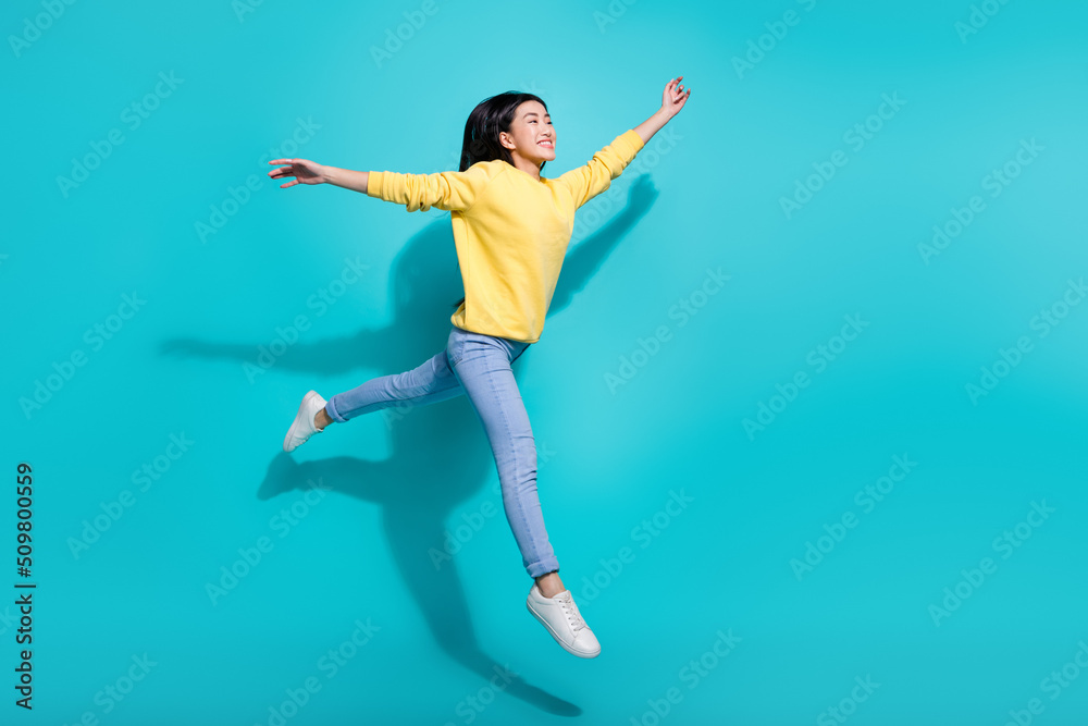 Full length photo of sweet excited woman wear yellow pullover jumping high empty space isolated teal color background Full length photo of sweet excited woman wear yellow pullover jumping high empty space isolated teal color background