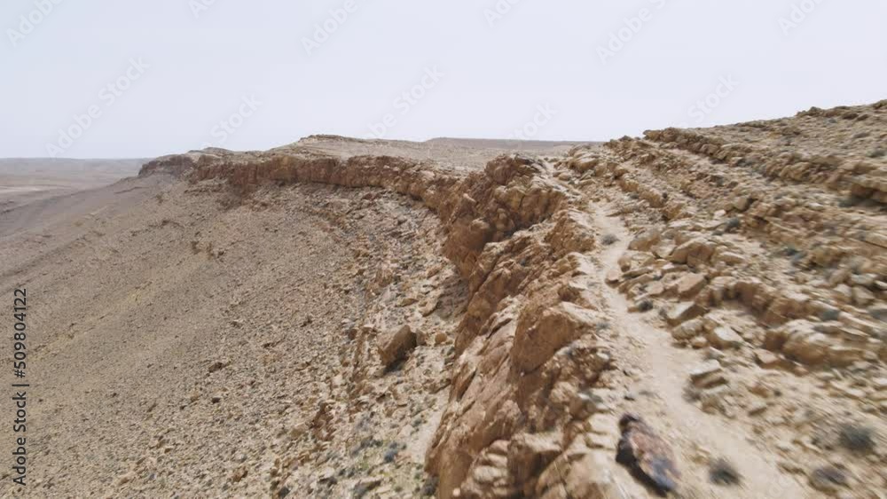 Dramatic drone shot of hiker in the desert walking along a high ridge next to a spectacular crater. Location is Mount Ramon and Ramon crater, Negev desert, Israel. Dramatic drone shot of hiker in the desert walking along a high ridge next to a spectacular crater. Location is Mount Ramon and Ramon crater, Negev desert, Israel.