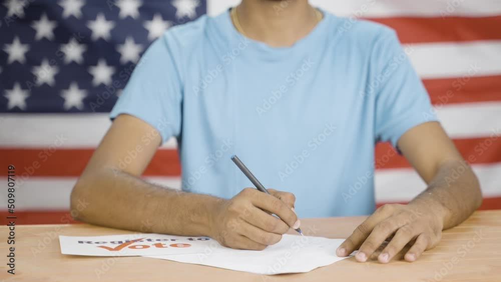 young man showing register to vote sign board while registering for election in front of US flag - cocept of voter registration young man showing register to vote sign board while registering for election in front of US flag - cocept of voter registration
