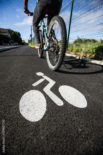 Piste cyclable avec un cycliste le long d'une route, la piste est séparée par un trottoir, le sol possède un marquage blanc pour indiquer le sens des vélos