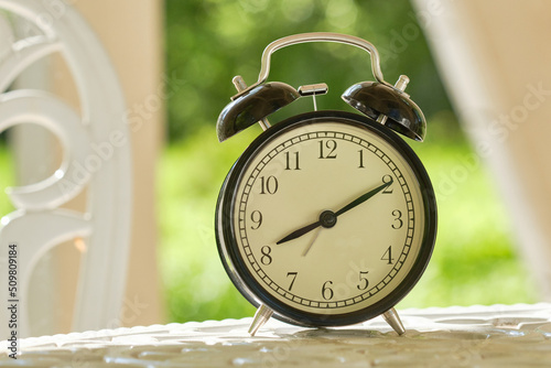 Retro alarm clock on a white table in garden against  blur green garden background. Shallow depth of field photo