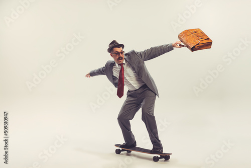 Tela Young funny man, businessman dressed in suit in 50s, 60s fashion style rides skateboard isolated on white background