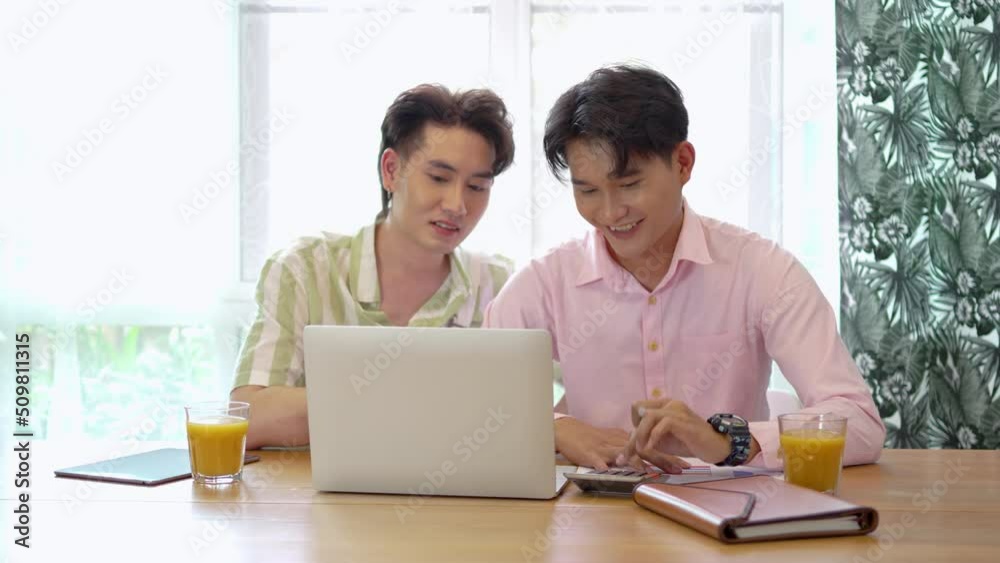 Asian businessman gay work with smile and laugh in office. Attractive male lgbtq collegues working together with using laptop pc and paper showing graphic chart in living room, Lgbt love concept Asian businessman gay work with smile and laugh in office. Attractive male lgbtq collegues working together with using laptop pc and paper showing graphic chart in living room, Lgbt love concept