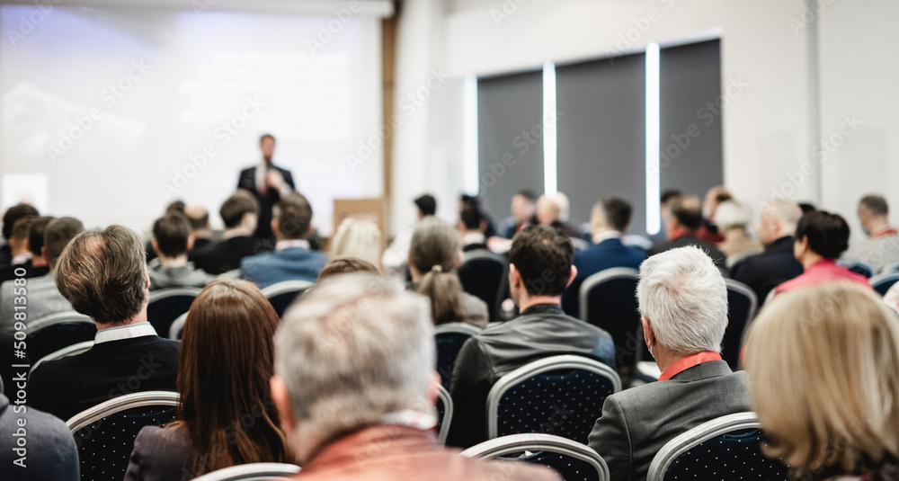 Fototapeta premium Speaker giving a talk in conference hall at business event. Rear view of unrecognizable people in audience at the conference hall. Business and entrepreneurship concept.