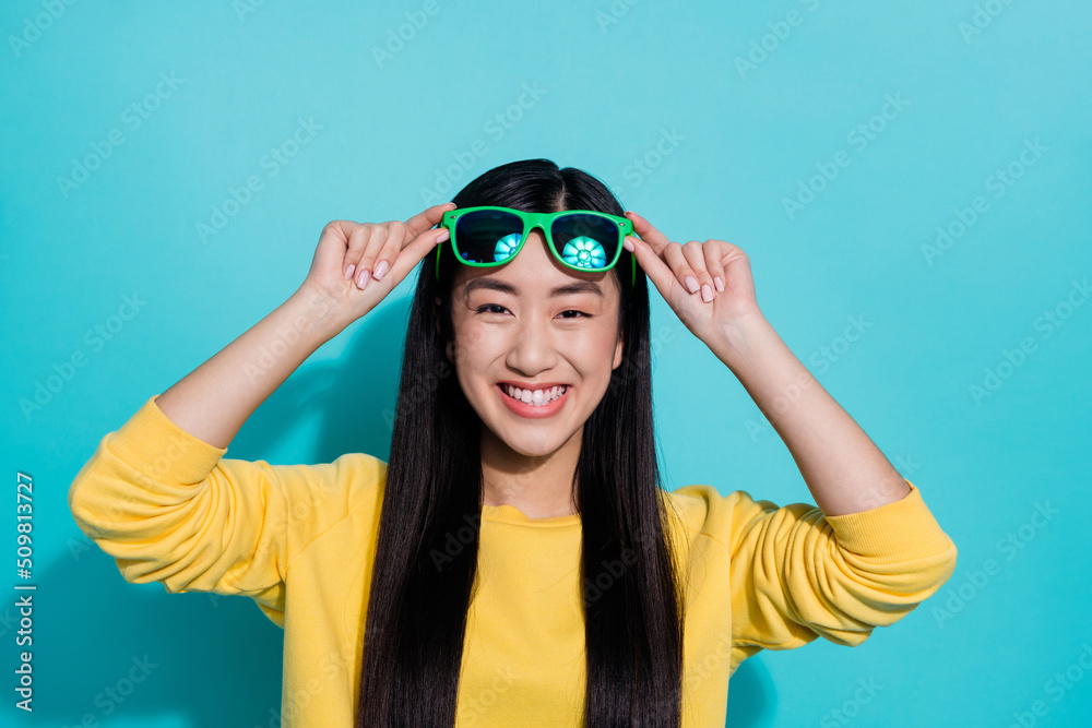 Photo of funny charming woman wear yellow pullover arms dark spectacles smiling isolated teal color background Photo of funny charming woman wear yellow pullover arms dark spectacles smiling isolated teal color background