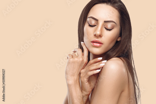 Beautiful young woman with clean perfect skin. Portrait of beauty model with natural nude make up and touching her face. Spa, skin care and wellness. Copyspace.