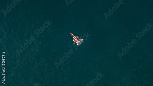 Woman with rubber ring, woman is swimming in the midle of the sea, Drone shot of the woman on the rubbel ring, Girl swims on rubbel ring, photo of girl from drone, girl in the oacen © Evgeniia