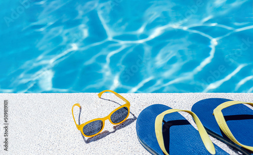 back view of flip flops and goggles on the white border of a swimming pool with bluish water in the background. vacation and summer concept.