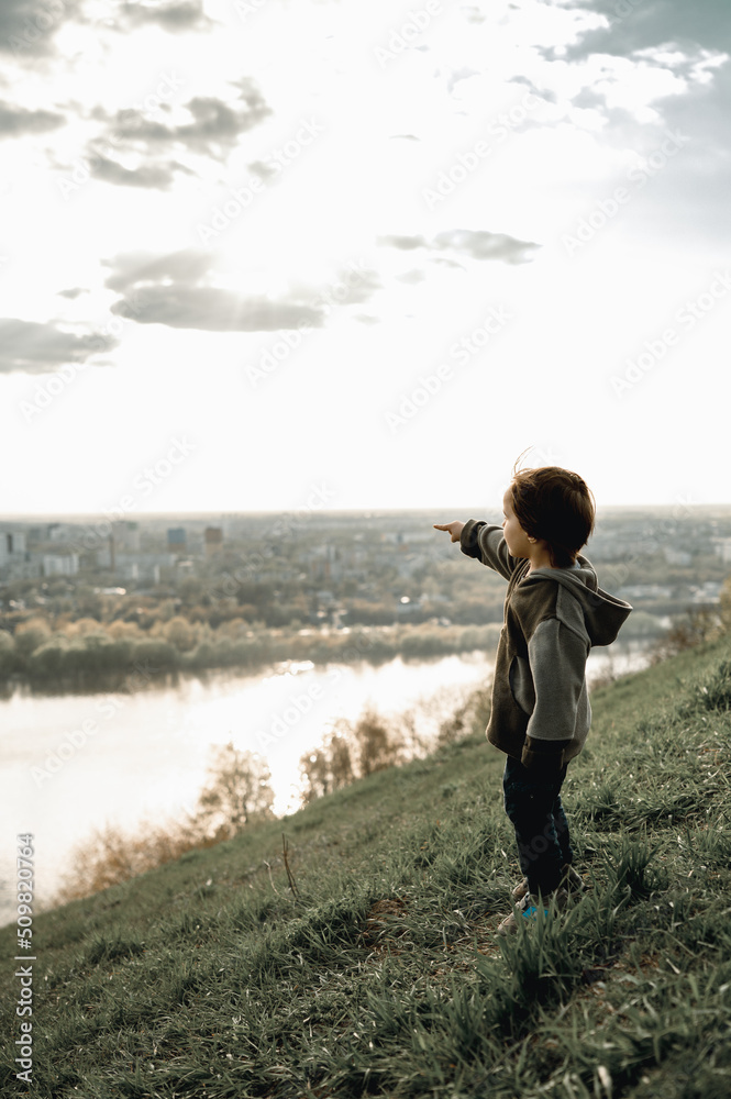 a child stands on a mountain and looks at the river