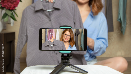 A woman blogger shows fashionable clothes taking pictures on a mobile phone. Online sales using smartphone. Influencer at work.