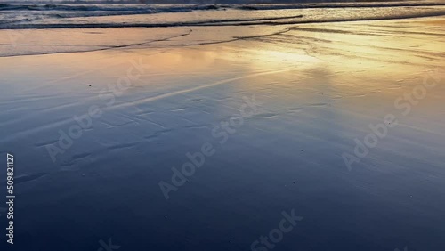 Beautiful golden sunset light reflecting in blue wet sand with tidal waves of the ocean rolling on shore. Natural background for design. Seaside wallpaper. photo