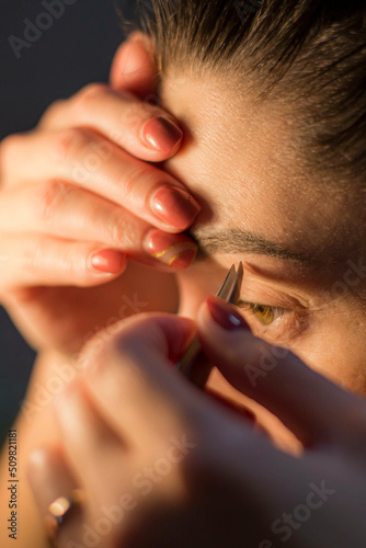 a natural girl at home plucks her eyebrows and paints her eyes, the front and background are blurred with a bokeh effect