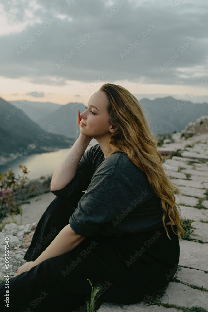 Woman on top of the mountain, view of the city and the sea. The girl looks at nature and enjoys, a tourist on a journey.