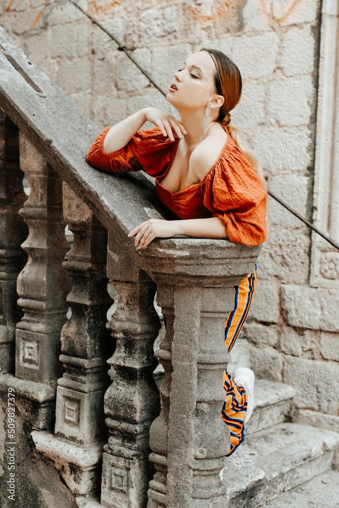 Gorgeous portrait of a beautiful woman in the old city on the stairs. Girl with makeup and hairstyle, long silver earrings posing.