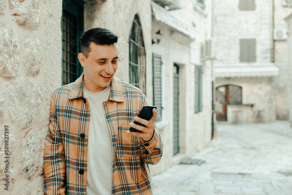 Portrait of a guy on the background of the old city with a phone. The guy writes a message and looks at the smartphone. Communication abroad, roaming, dating while traveling.