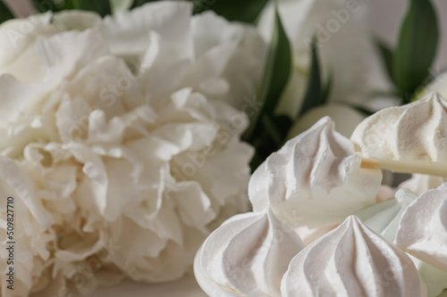 Bouquet of white peonies on a white background and white meringue cookies.