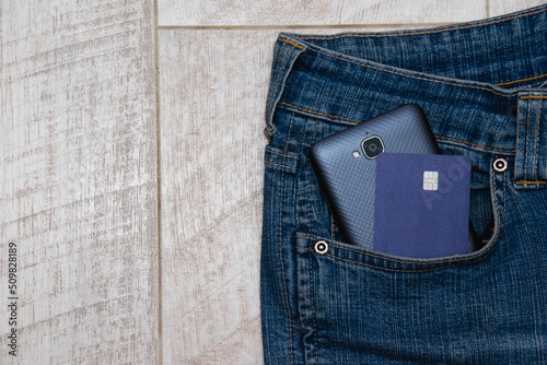 Bank card and smartphone in jeans pocket on light wooden background, copy space on the left