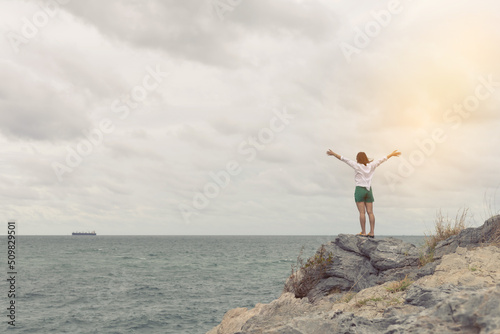 Woman standing with arms spread out on the rocks by the sea.