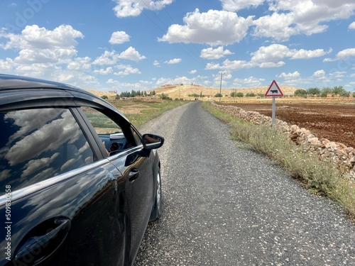 black car riding on asphalt road leads on valley under beautiful sky in a sunny day
