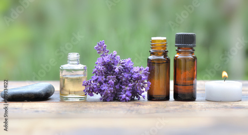 bottles of essential oil and lavender flowers in line on a table and on green...