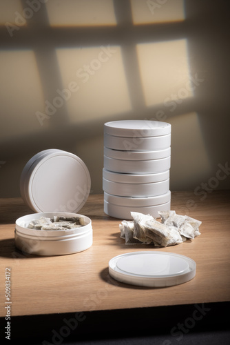 Studio shot of white swedish smokeless tobacco cans and portion snus pouches on a wooden table.