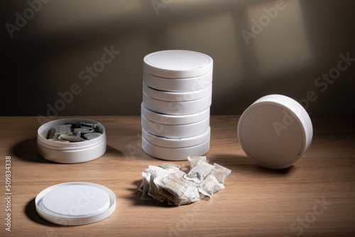 Studio shot of white swedish smokeless tobacco cans and portion snus pouches on a wooden table.