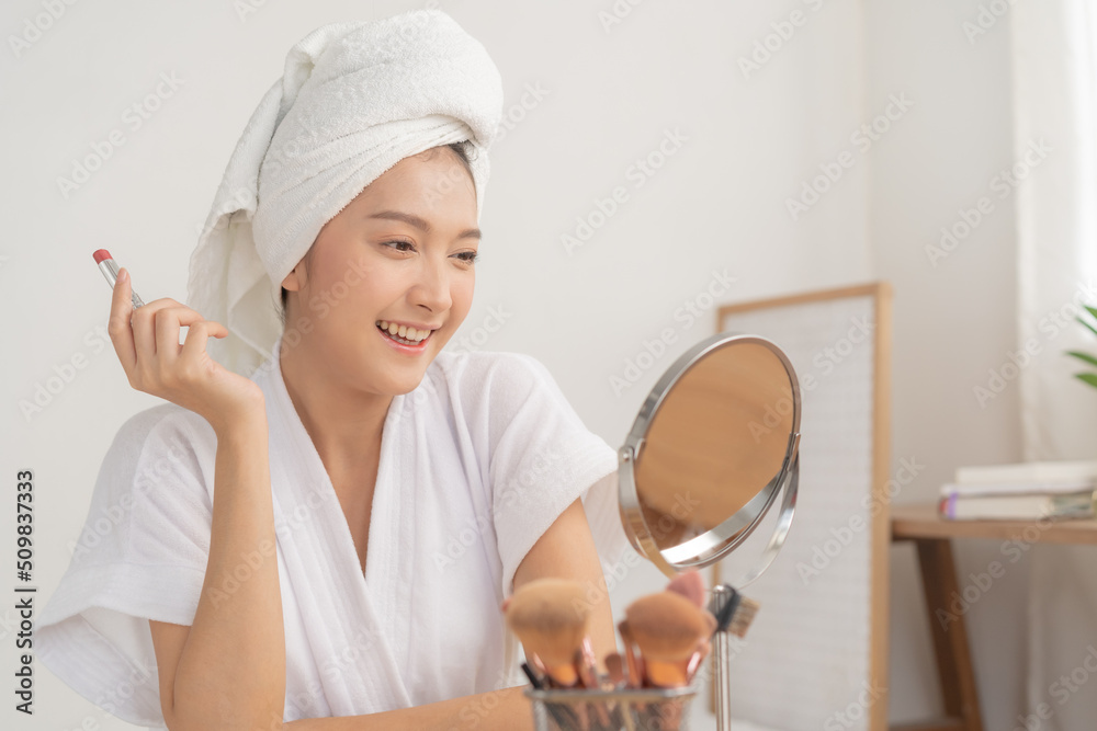 Beauty cosmetics concept, asian young woman, girl in bathrobe, towel after shower bath at home make up face by applying lipstick, lips on her mouth, looking at the mirror, fashion style, skin care. Beauty cosmetics concept, asian young woman, girl in bathrobe, towel after shower bath at home make up face by applying lipstick, lips on her mouth, looking at the mirror, fashion style, skin care.