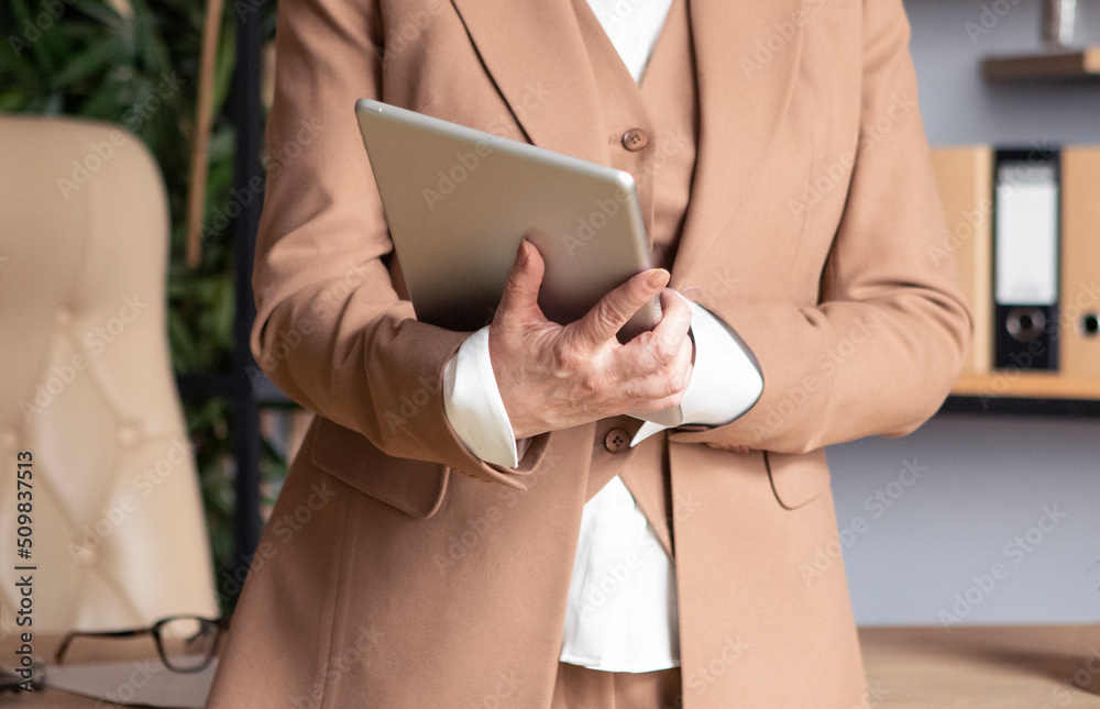 business woman in a beige suit working at the office, typing on tablet