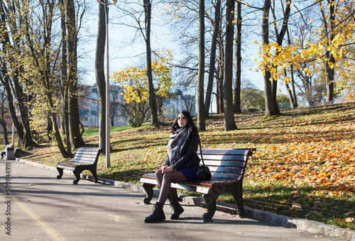 young girl sits on bench in city park on autumn day © Radnatt