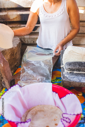 Mujer mexicana torteando maza de maíz en un metate y una estufa de leña para hacer tortillas caseras	
 photo