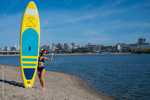 Caucasian woman walks along the beach and carries a sup board on the river in the city. Summer sport.