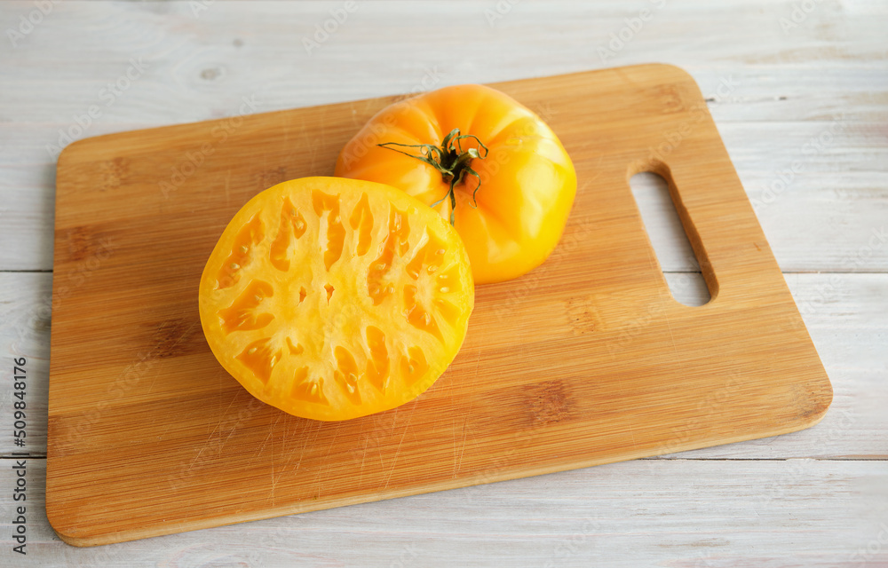 Big fresh yellow tomato cut in half on a wooden cutting board. Selective focus. Close up. Concept of healthy, useful and organic products. Top view