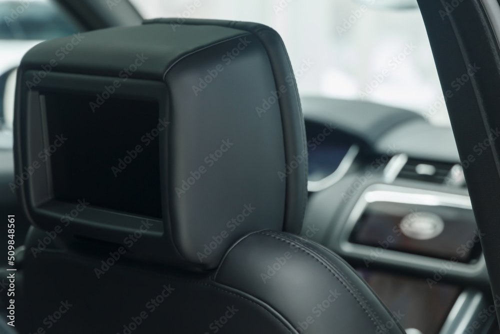 The car is inside. View from the back seat to the car control panel. The interior of a prestigious luxury modern car. Focus on the TV display in the seat headrest. Close-up