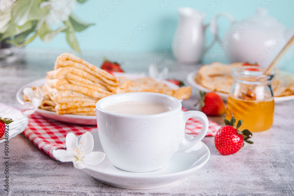 Cup of tea and homemade tasty crepes with fresh strawberries with honey. Breakfast concept.