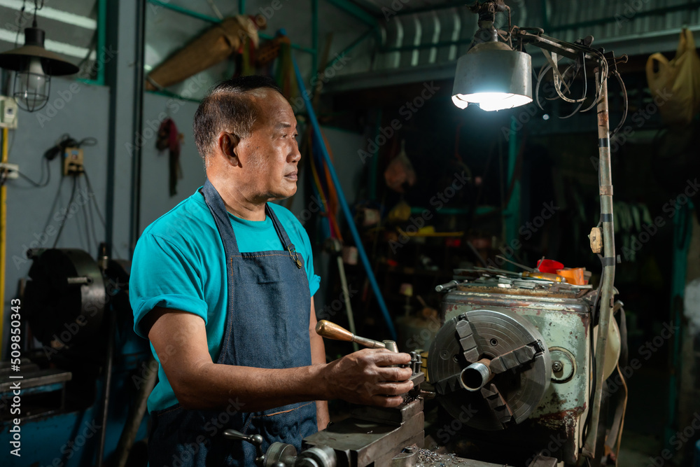 Portrait of a senior Asian man who is a steelworker. using a small steel turning tool to prepare for a lathe job in my family's small lathe.