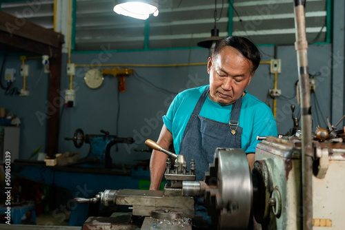 Portrait of a senior Asian man who is a blacksmith. Inspecting small steel turning tools. to prepare the lathe In the family's small lathe