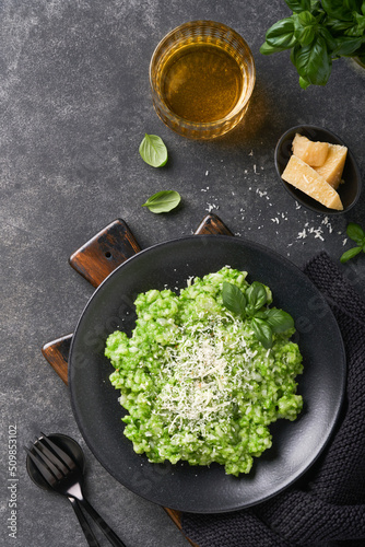 Italian risotto. Delicious risotto with pesto sauce or wild garlic pesto, basil, parmesan cheese and glass of white wine on dark slate table background. Italian dinner. Top view with copy space.